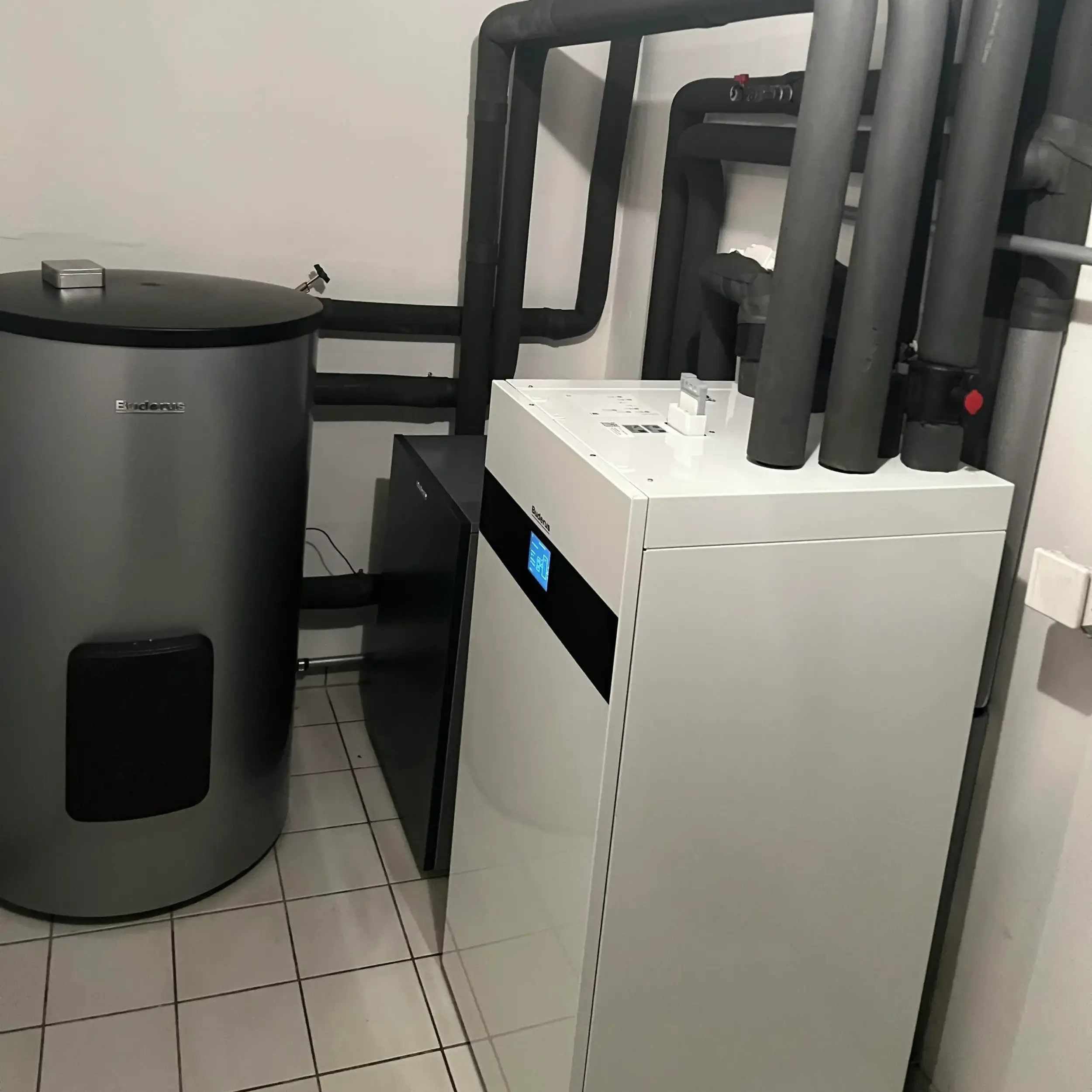 Technikraum mit neu installierter Wärmepumpen-Inneneinheit und Warmwasserspeicher